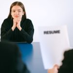 Candidata participa de entrevista de emprego diante de dois recrutadores, com o currículo sobre a mesa.
