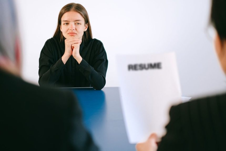 Candidata participa de entrevista de emprego diante de dois recrutadores, com o currículo sobre a mesa.