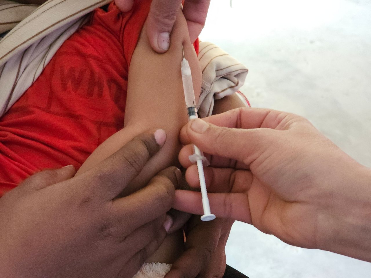 Profissional de saúde aplica uma vacina em uma criança dentro de uma unidade de atendimento.