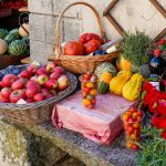 Banca ao ar livre com frutas, legumes e verduras frescos, incluindo maçãs, tomates, abóboras e ervas.