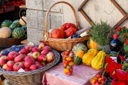 Banca ao ar livre com frutas, legumes e verduras frescos, incluindo maçãs, tomates, abóboras e ervas.