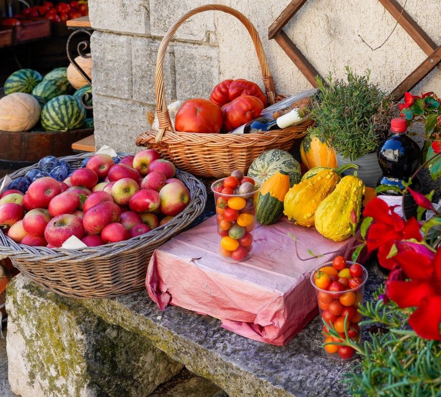 Banca ao ar livre com frutas, legumes e verduras frescos, incluindo maçãs, tomates, abóboras e ervas.