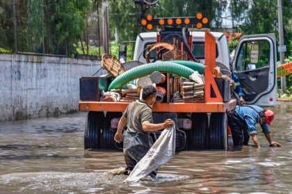 Trabalhadores caminham por uma área alagada próxima a um caminhão durante uma operação urbana após chuva intensa.