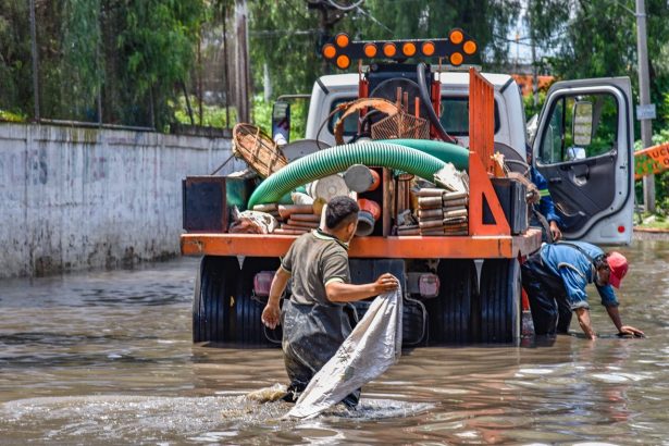Trabalhadores caminham por uma área alagada próxima a um caminhão durante uma operação urbana após chuva intensa.